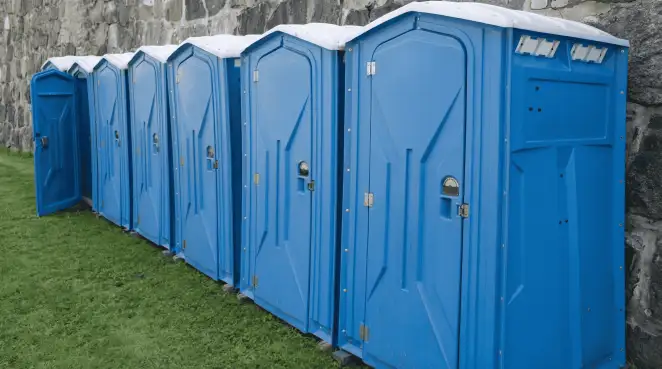 Row of blue portable toilets lined up on grass against a stone wall for event sanitation in Baton Rouge, LA